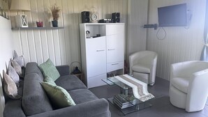 A modern living room with a grey sofa, white armchairs, a glass coffee table, and a white cabinet with speakers. - Cottage in Bourbonnais countryside with private garden (Meillard)