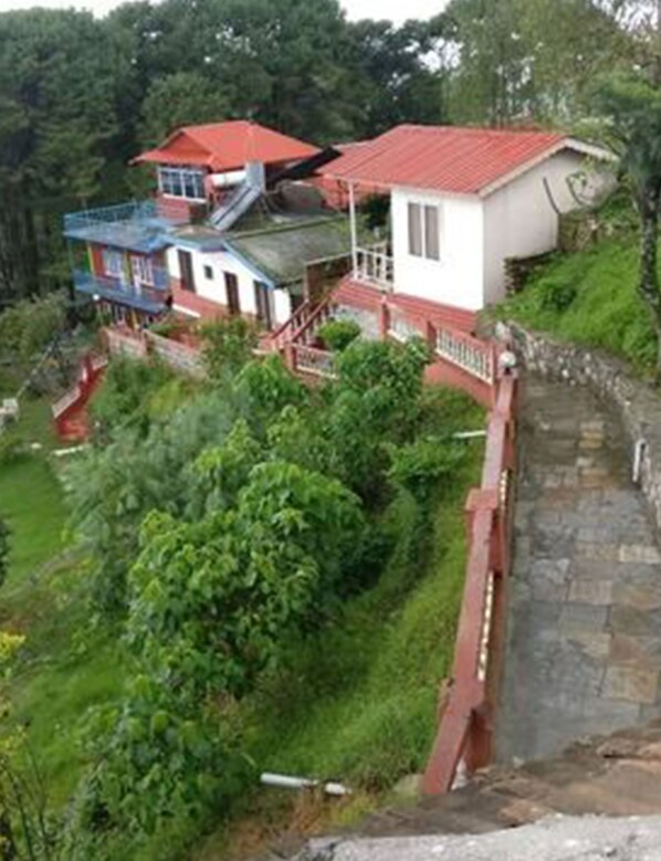 Una propiedad en una ladera con varias construcciones, incluyendo una casa principal con techo rojo y una estructura más pequeña con techo azul.