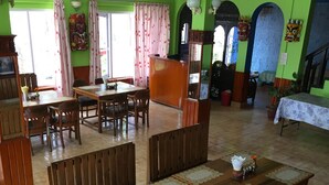 A dining area with wooden tables and benches, green walls, and a large plant in the foreground. - Hotel Galaxy View Tower (Baluwapati Deupur)