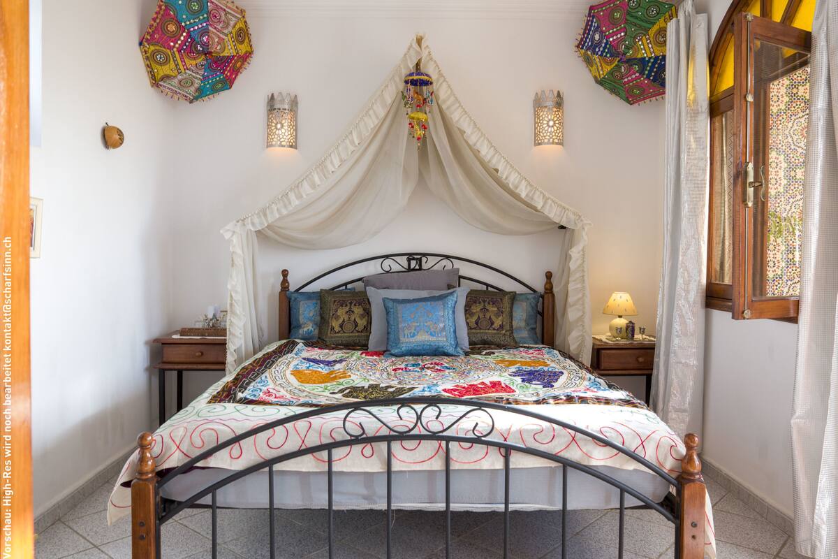 Una cama con dosel, almohadas decorativas y un edredón colorido.