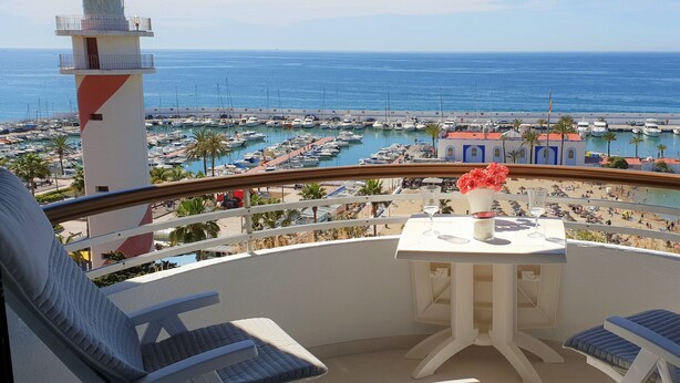 A balcony with a table and chairs, overlooking a marina with boats and a beach. - Fantastic 2 bed 2 bath beachside penthouse with pool and parking (Marbella)