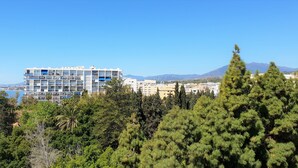 A multi-story hotel with balconies overlooking a coastal area, surrounded by dense greenery and mountains in the background. - Fantastic 2 bed 2 bath beachside penthouse with pool and parking (Marbella)
