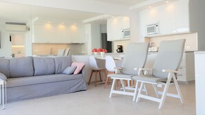 A modern living room with a grey sofa, white armchairs, and a kitchen area in the background. - Fantastic 2 bed 2 bath beachside penthouse with pool and parking (Marbella)