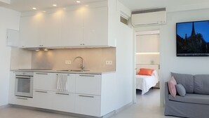 A modern kitchen with white cabinets, a stainless steel range hood, and a built-in oven. There is a dining area with a grey sofa and a painting of Notre-Dame Cathedral. - Fantastic 2 bed 2 bath beachside penthouse with pool and parking (Marbella)