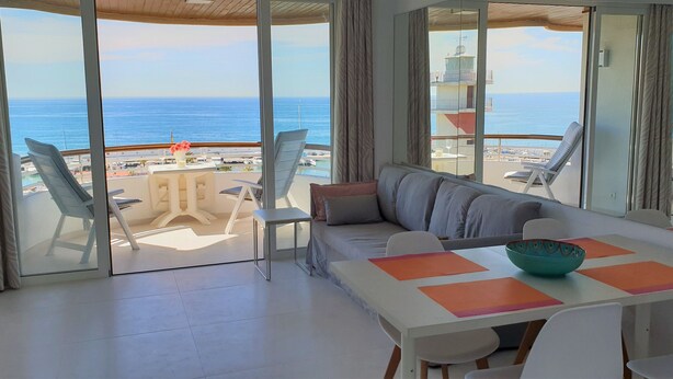 A modern living room with a large glass door leading to a balcony with a view of the sea and a beach. - Fantastic 2 bed 2 bath beachside penthouse with pool and parking (Marbella)