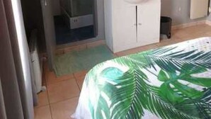 Een hotelkamer met een bed, een badkamer met douche, wastafel en spiegel.