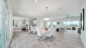 A spacious kitchen with modern appliances, a dining area with white chairs, and a large window offering a view of the outdoors. - 30A Retreat - 2 Homes, Gulf Views, Great for Large Groups! (Santa Rosa Beach)