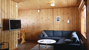 Interior acogedor de una cabaña con techo de madera, un televisor de pantalla plana en la pared, un sofá azul oscuro y una pequeña mesa redonda.