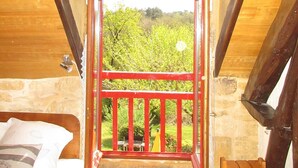A bedroom with a wooden ceiling, a stone wall, and a view of greenery outside. - Domaine de l'Homme: The Red House with swimming pool (ST VINCENT LE PALUEL)