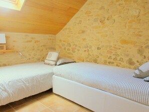 A small, cozy room with two single beds, a stone wall, and a wooden ceiling.