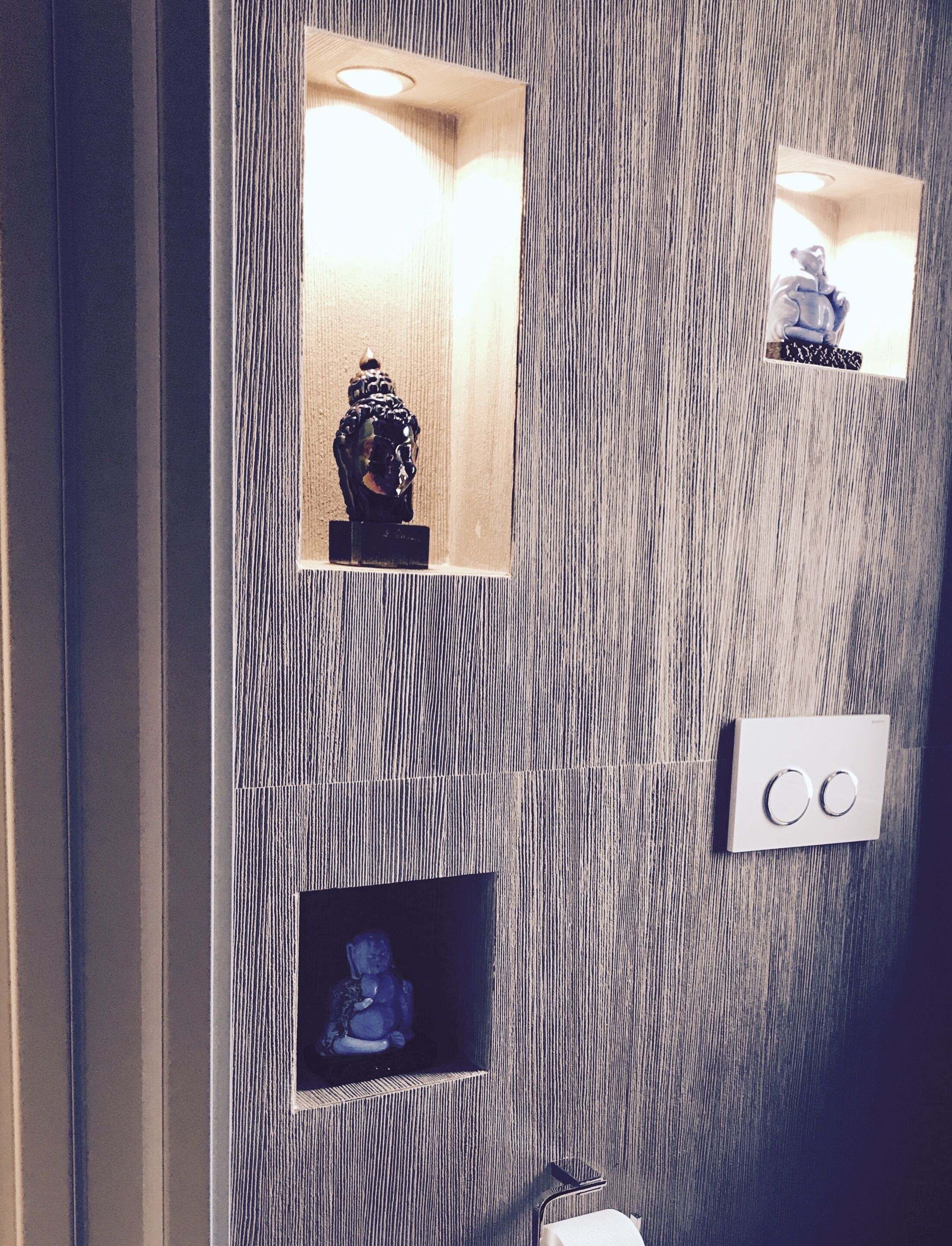 A wall with three recessed shelves displaying statues, a light switch, and a mirror.