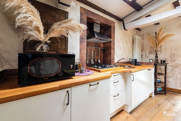 Une cuisine moderne avec des meubles blancs, un plan de travail en bois, un micro-ondes noir et une cuisinière à gaz.