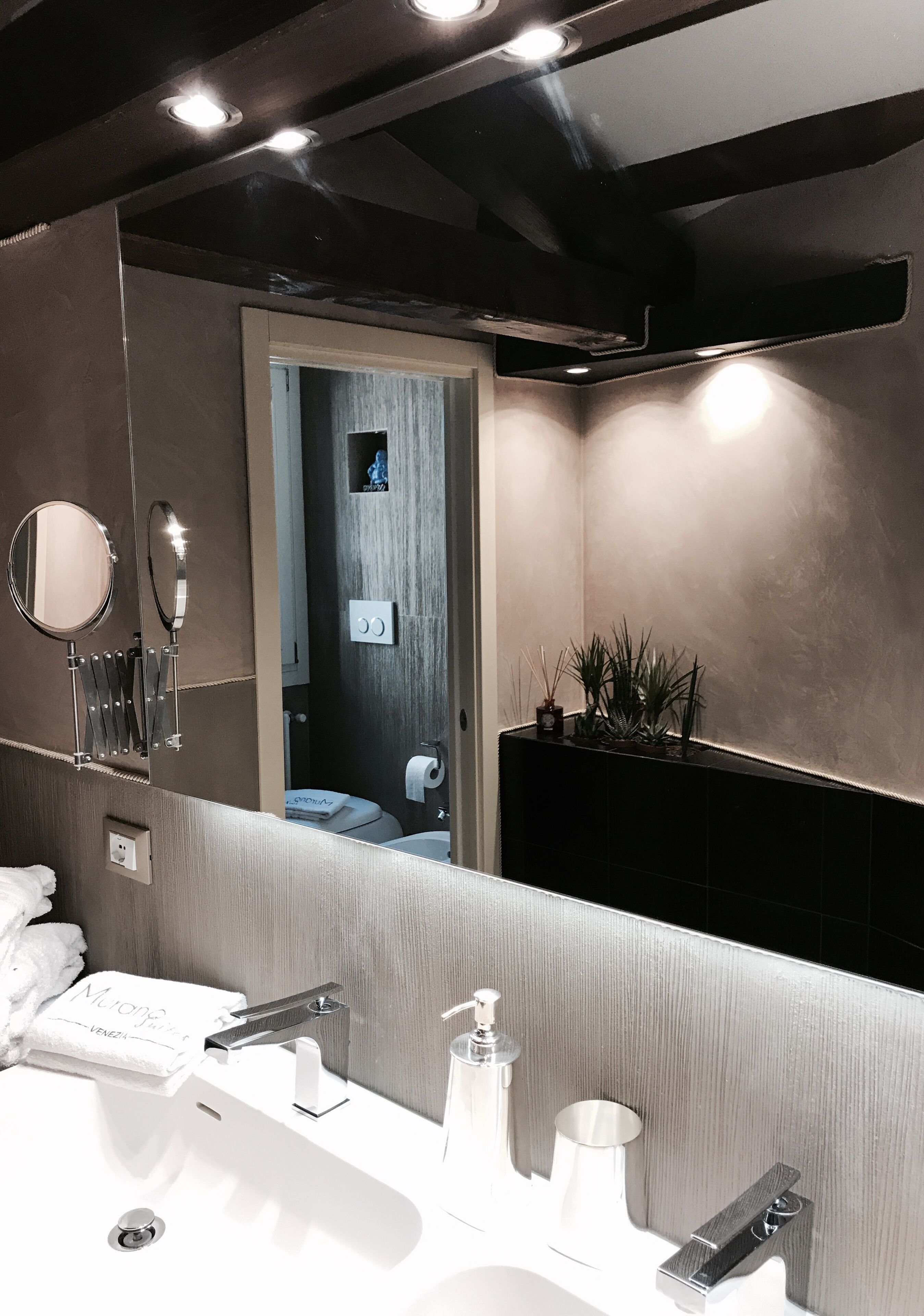 A modern bathroom with a large mirror, a sink with a faucet, a towel, and a plant on the wall.