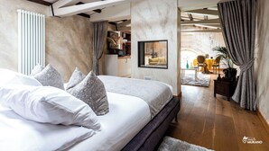 Een slaapkamer met een groot bed, een houten bankje, een radiator en uitzicht op een eetruimte.