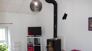 A living room with a TV on a white stand, a black fireplace, a wooden coffee table, a black sofa, and a hanging light fixture.