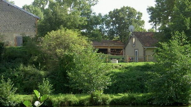 A house with a brick exterior, surrounded by lush greenery and a pond.