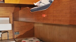 Un lit superposé avec une tête de lit en bois, une petite fenêtre et un luminaire fixé au mur.