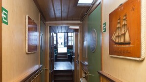 Un couloir étroit aux murs en bois, avec une porte verte sur le côté droit. Deux panneaux verts sont fixés au mur gauche, l’un au-dessus de l’autre.