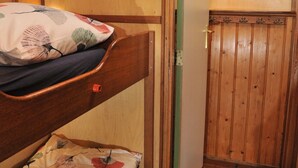 Un lit superposé avec un oreiller et une petite table, une porte avec une poignée et un tableau encadré accroché au mur.