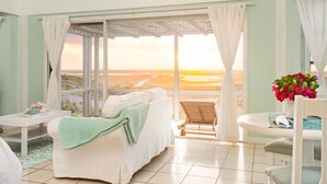 A room with a view of the beach, a white sofa, a small table, and a chair. - Sunset Cottage at The Dragon Cay Resort  (Conch Bar)