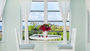 A room with two white chairs, a round table with a vase of flowers, and a view of greenery and the sea through large windows. - Sunset Cottage at The Dragon Cay Resort  (Conch Bar)
