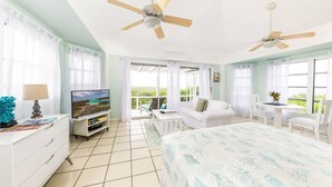 A hotel room with a bed, a TV, a desk, and a balcony with a view. - Sunset Cottage at The Dragon Cay Resort  (Conch Bar)