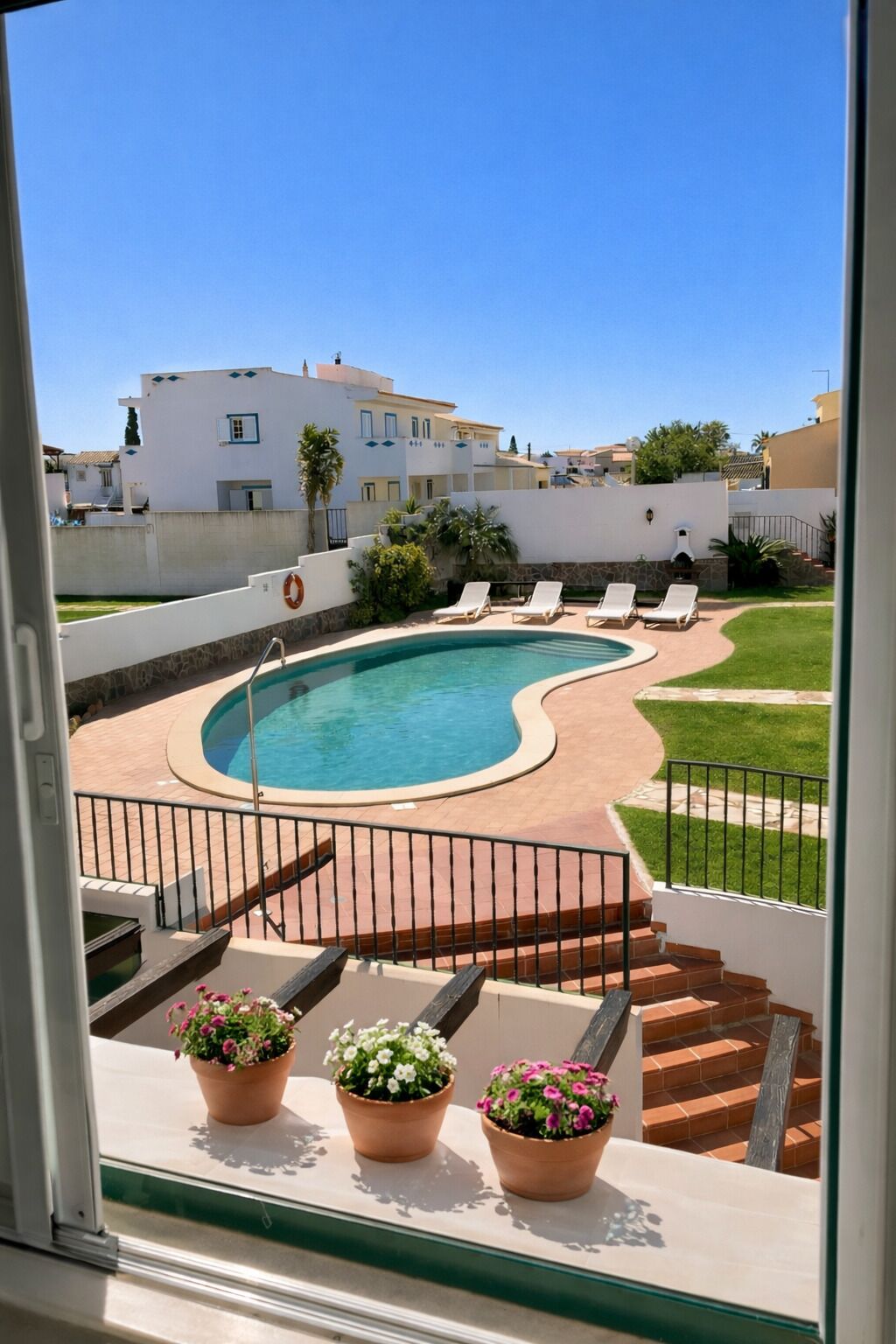 A swimming pool with lounge chairs, a stone deck, and a view of white buildings.