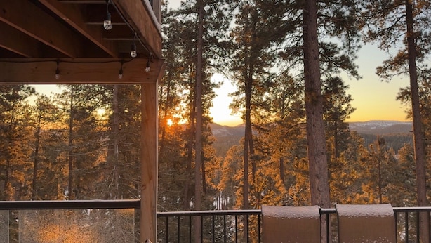 En träveranda med utsikt över en skog och en solnedgång.