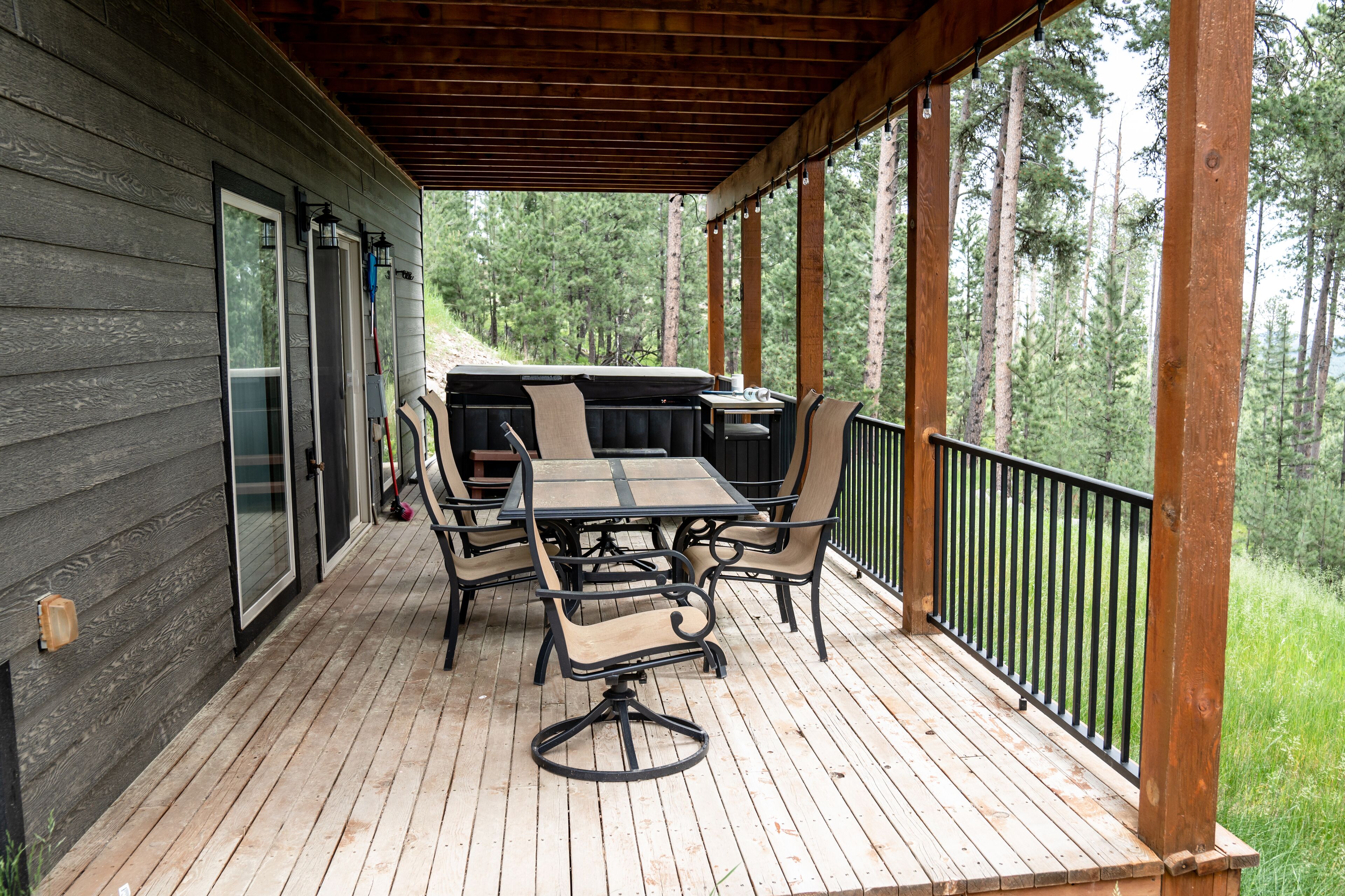 Un patio techado al aire libre con mesa y sillas de madera, una parrilla y vistas a un área boscosa.