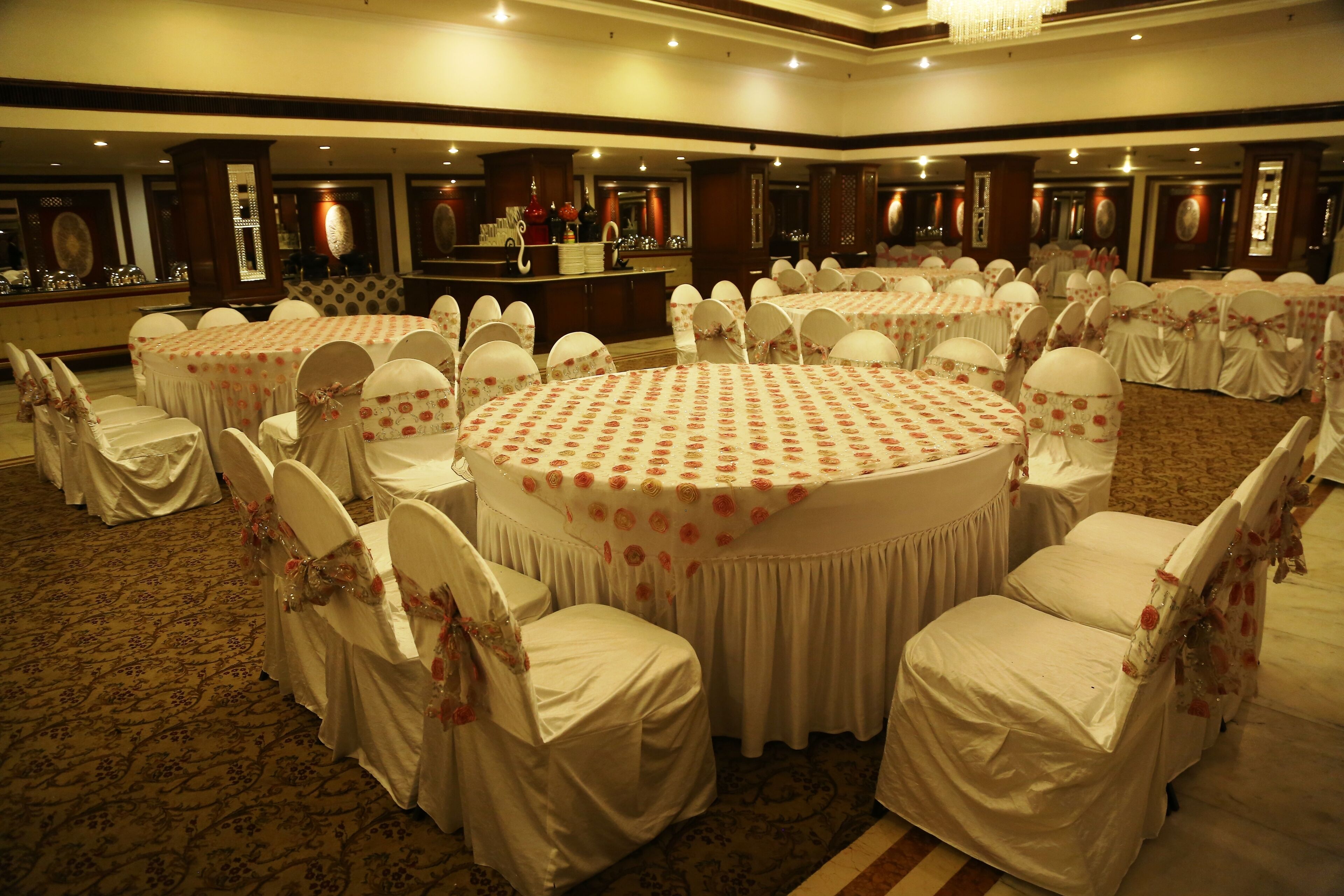 A banquet hall with round tables covered in white tablecloths and chairs with white covers and pink floral sashes.