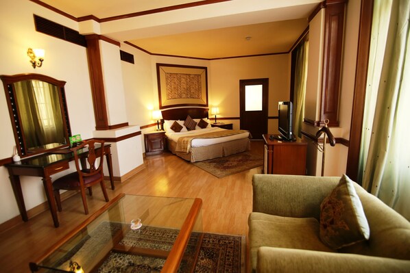 Una habitación de hotel con cama, sofá, escritorio, silla, televisor y espejo.