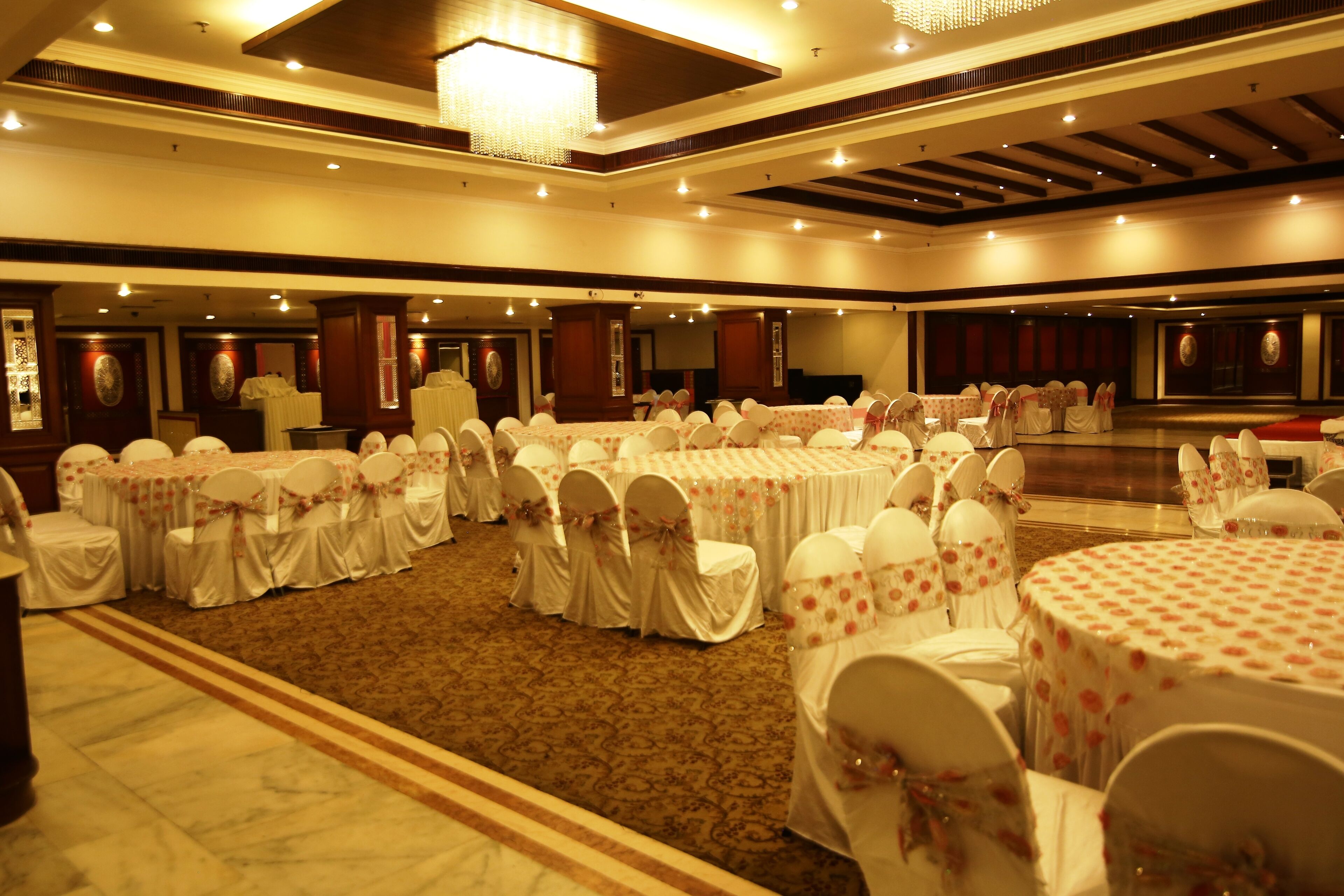 A large banquet hall with round tables covered in white tablecloths and chairs with white covers and bows.