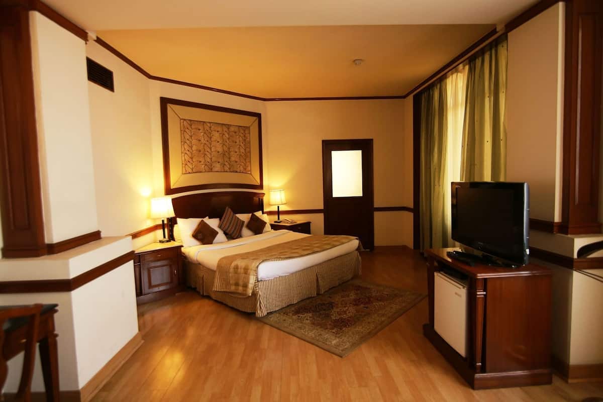 A hotel room with a bed, bedside tables, a television, a rug, and a door.