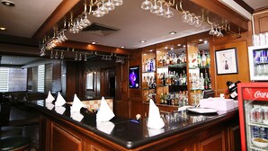 A bar area with a counter, bar stools, and a display of various bottles and glasses. - Hotel President (Jalandhar)