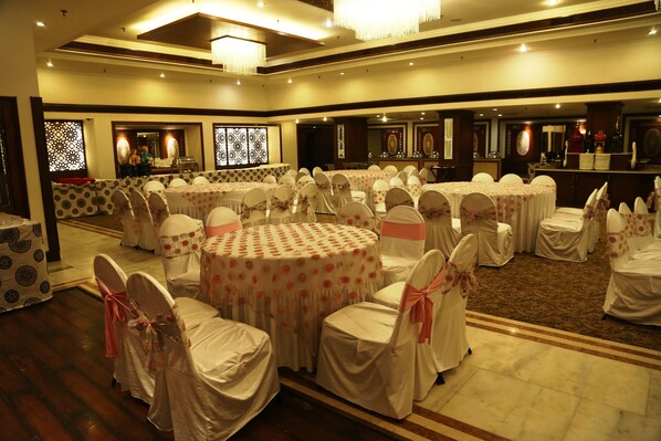 Un salón de banquetes con mesas redondas cubiertas con manteles blancos y sillas con cintas rosas.