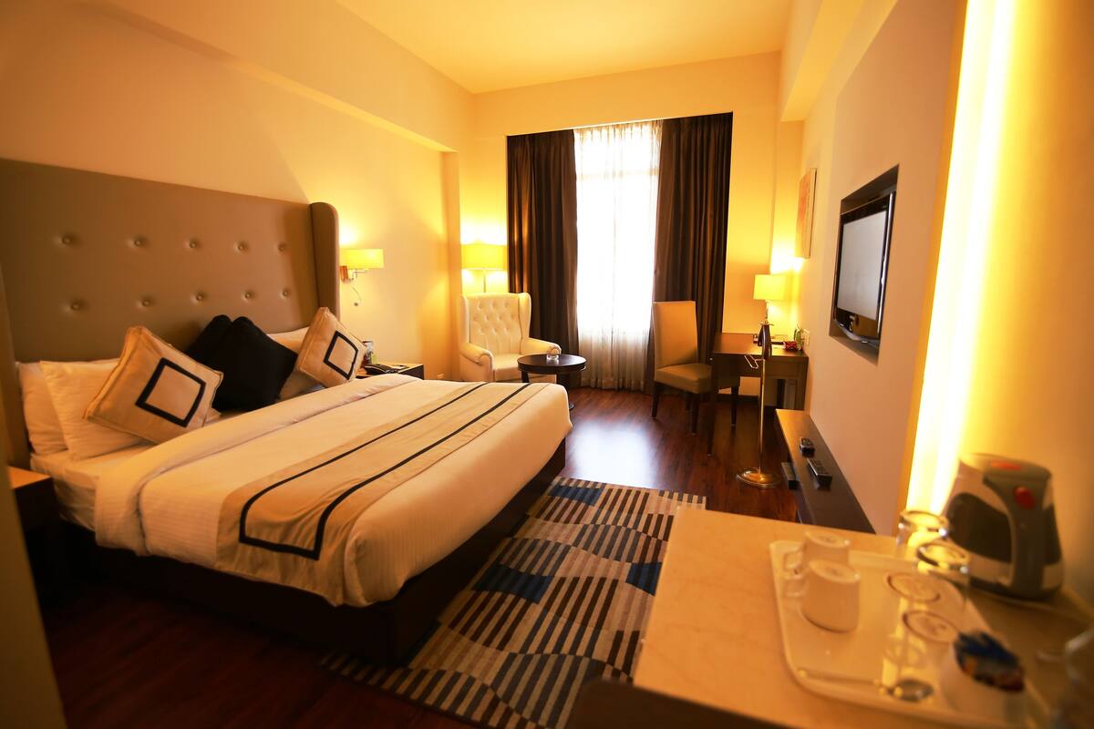 A hotel room with a large bed, a desk with a chair, a TV, and a window with curtains.