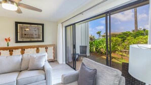 Un vaste espace de vie doté d’un ventilateur de plafond, d’un ensemble de canapés, d’une table à manger et offrant une vue sur un jardin luxuriant grâce à de grandes portes-fenêtres coulissantes.