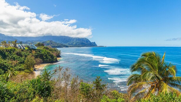 Un paysage côtier avec une plage, des vagues de l’océan et une chaîne de montagnes en arrière-plan.