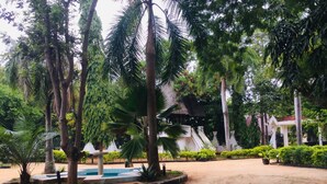 A landscaped area with palm trees, a central water feature, and a white building with a red roof in the background. - Emerald House (Dar es Salaam)