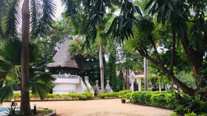 A thatched-roof gazebo surrounded by lush greenery and a paved area. - Emerald House (Dar es Salaam)