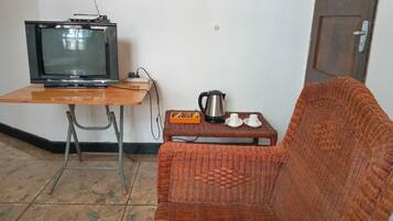 Une pièce avec un téléviseur posé sur une table en bois, une chaise en osier, une machine à café et deux tasses sur une petite table.