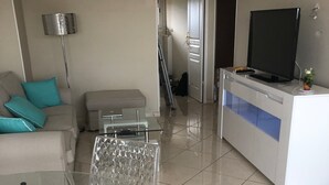 A modern living room with a sofa, a glass coffee table, a TV on a stand, and a hallway leading to another room. - 3 rooms apartment renovated with panoramic sea view (antibes)