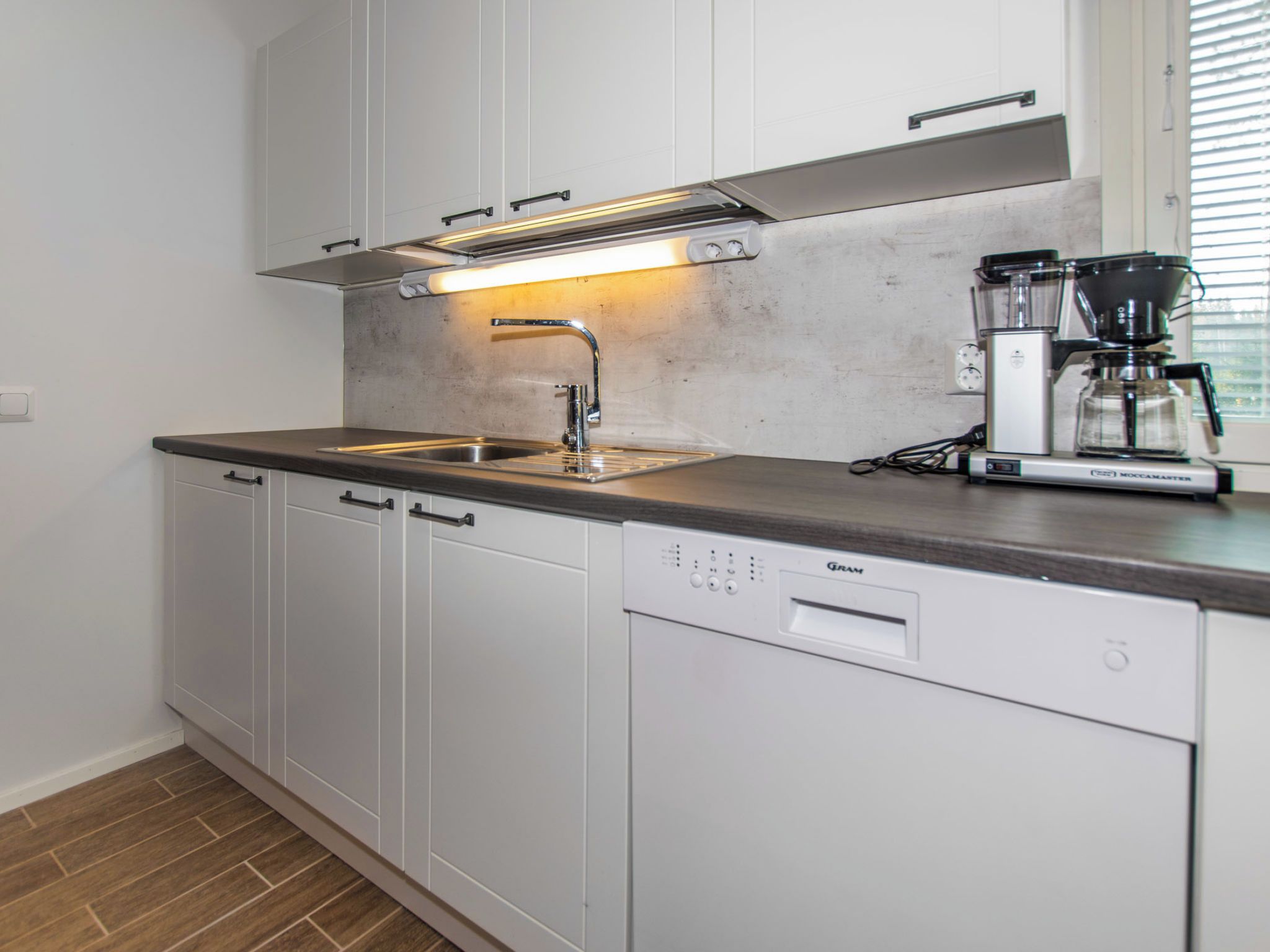 Una cucina moderna con lavastoviglie, macchina da caffè e una finestra con tende.
