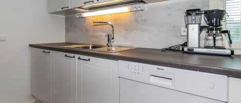Una cucina moderna con lavastoviglie, macchina da caffè e una finestra con tende.