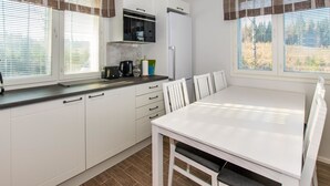 A compact kitchen with white cabinets, a microwave, and a refrigerator. There is a dining table with chairs and a window with blinds.