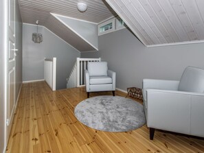 Una habitación con piso de madera, un tapete gris, un sillón blanco y un sofá blanco.