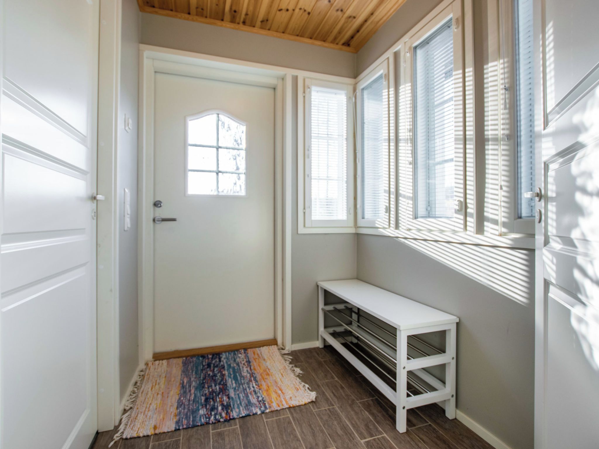 A hallway with a white door, a bench, and a window with blinds.
