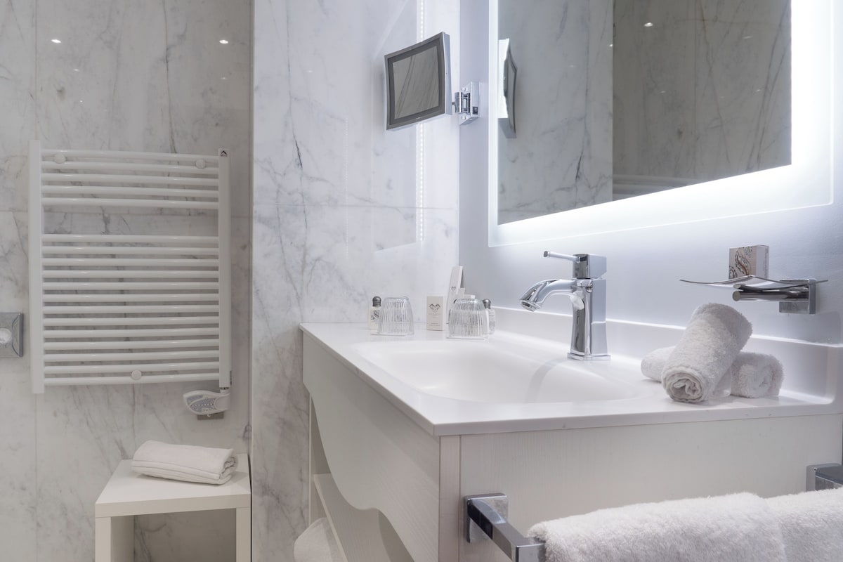 A modern bathroom with a white marble sink, a large mirror, and a towel rack.