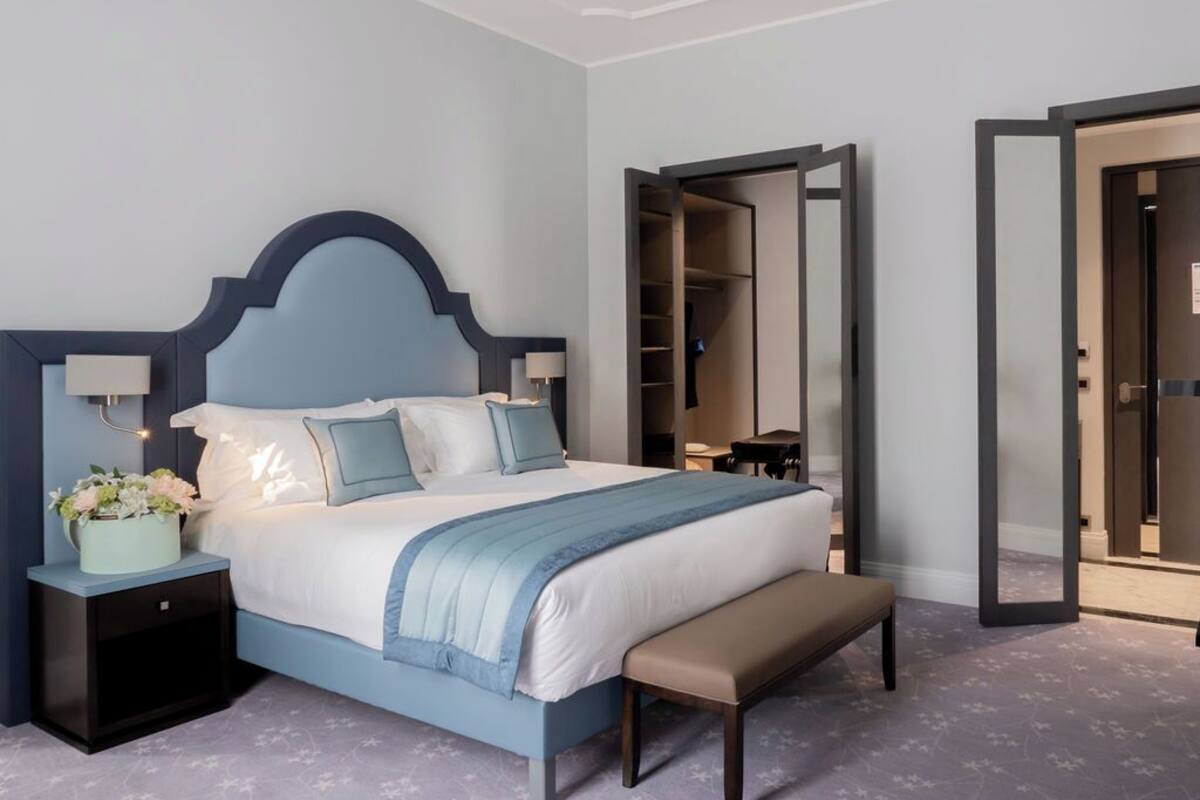 Une chambre à coucher comprenant un lit, des tables de chevet, un banc, un miroir et une armoire.