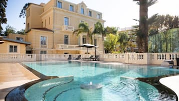 Una piscina al aire libre, sombrillas, sillones reclinables de piscina